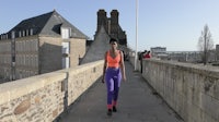 a woman walking on a bridge with buildings in the background