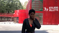 a woman in a black jacket standing in front of a red building