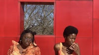 two women standing in front of a red wall